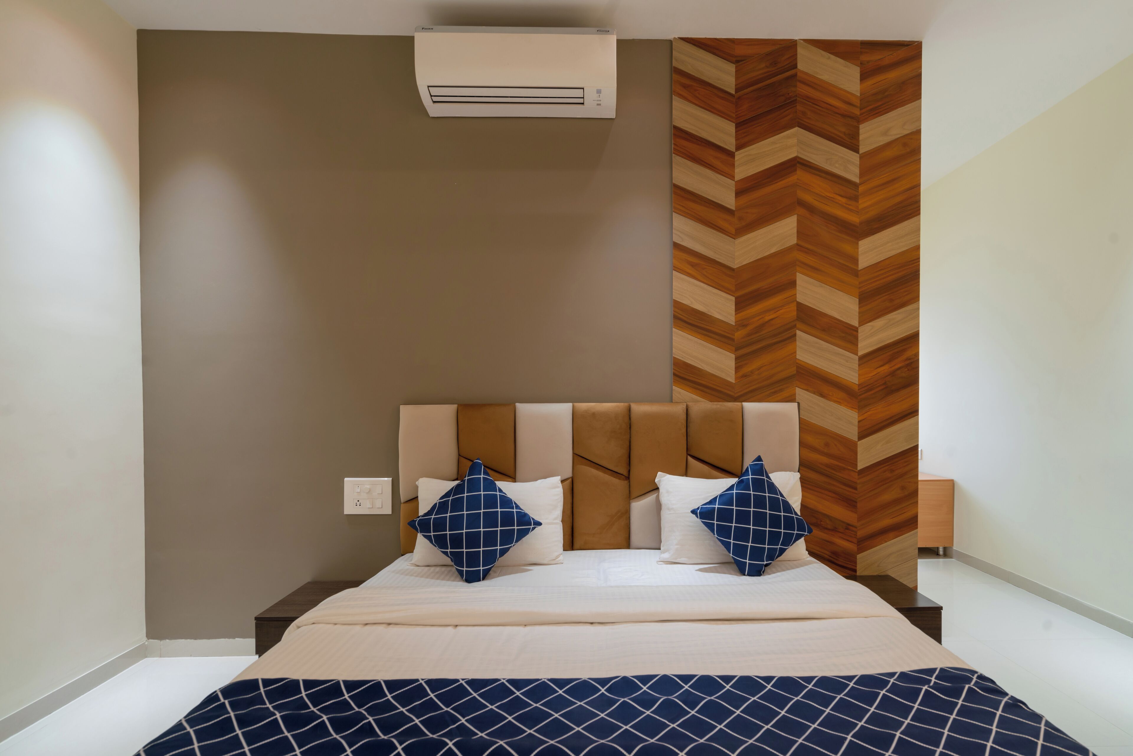 A bedroom with a bed, two pillows, a nightstand, an air conditioner, and a wooden wall panel.