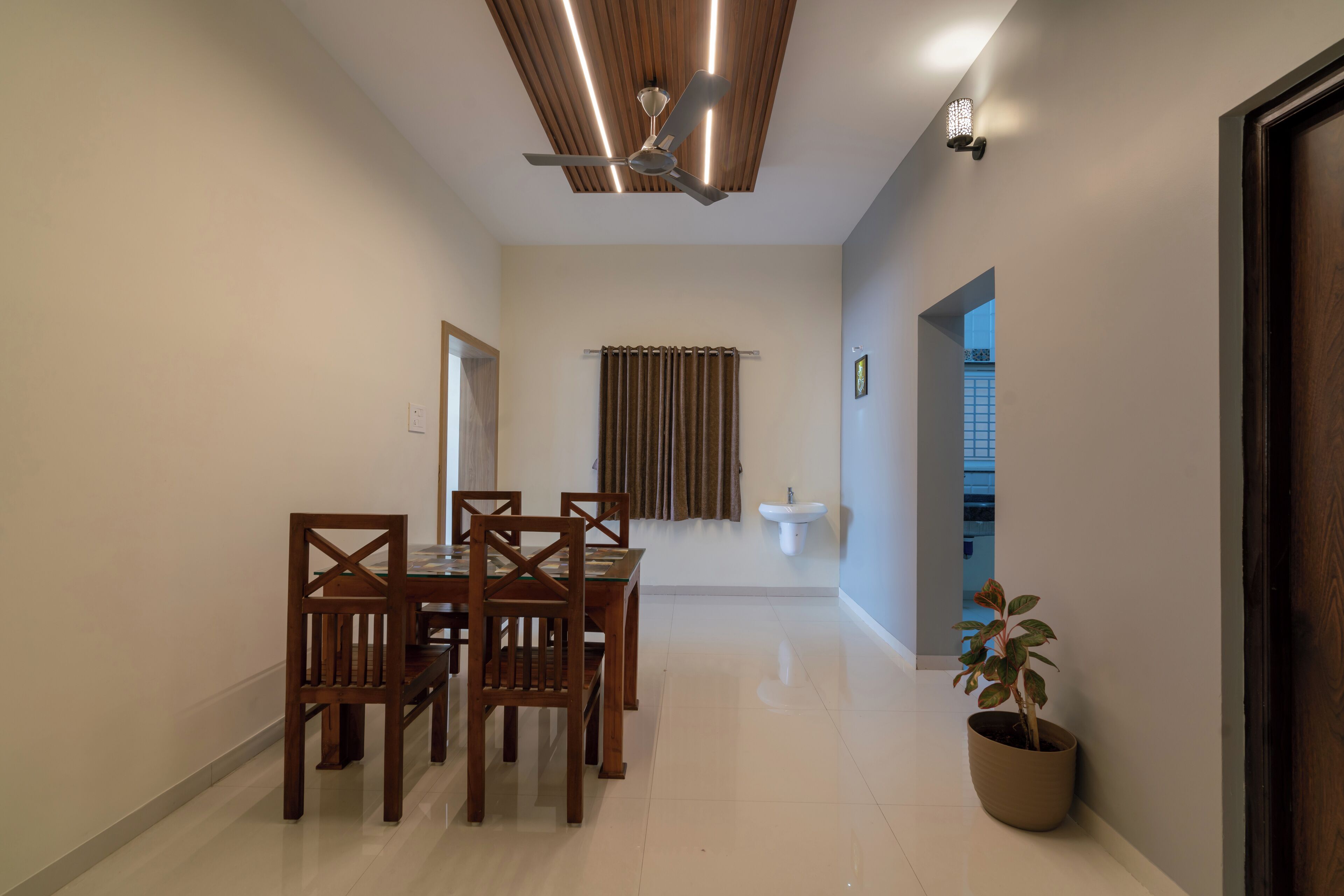 A dining area with a wooden table and chairs, a ceiling fan, a window with curtains, and a potted plant.