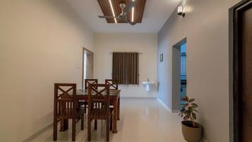 A dining area with a wooden table and chairs, a ceiling fan, a window with curtains, and a potted plant.