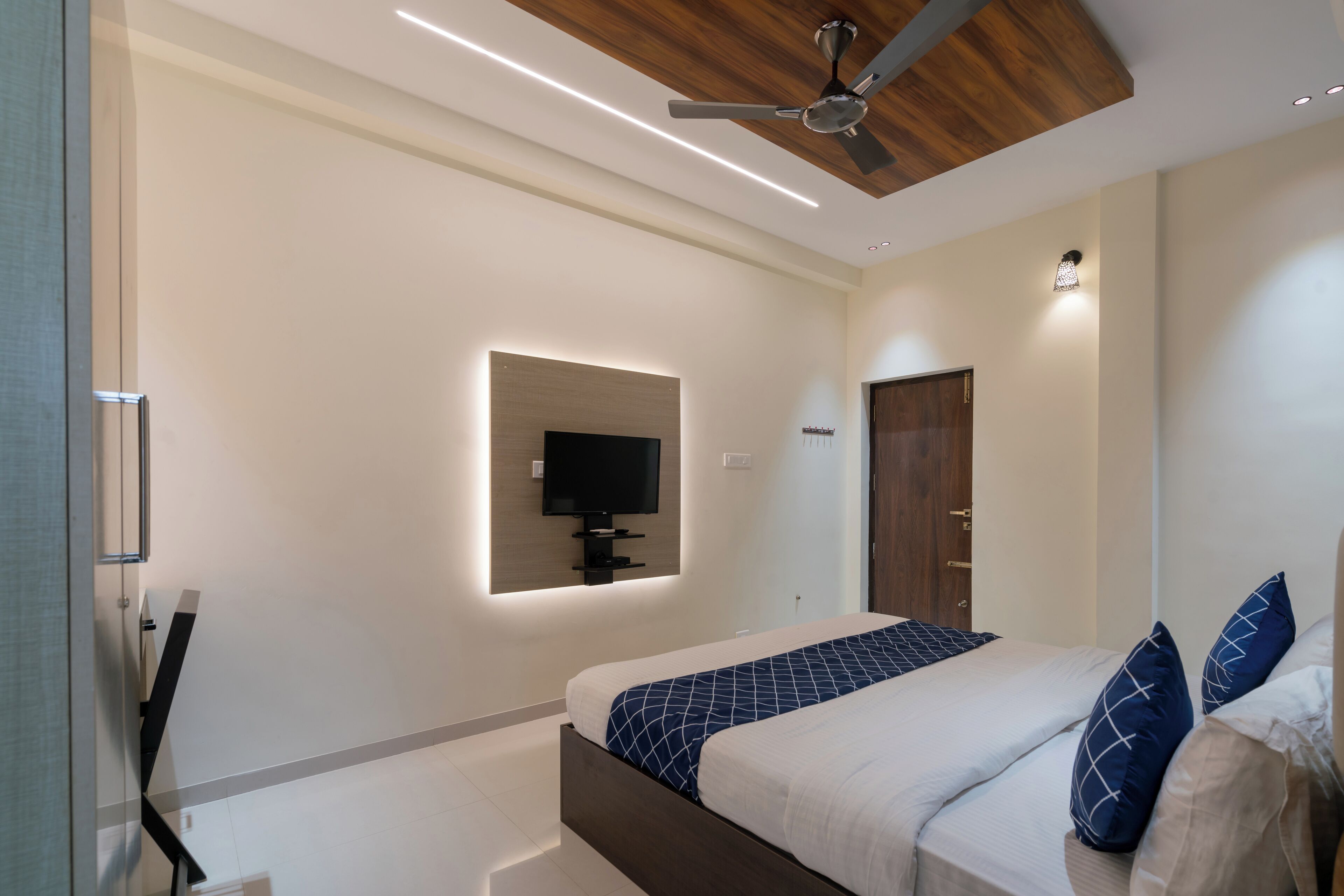 Quarto moderno com cama, ventilador de teto, iluminação embutida, TV na parede e uma porta.