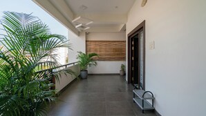 Un corridoio pulito e moderno, con pavimento piastrellato, piante in vaso, una panca e una porta con pannello decorativo.
