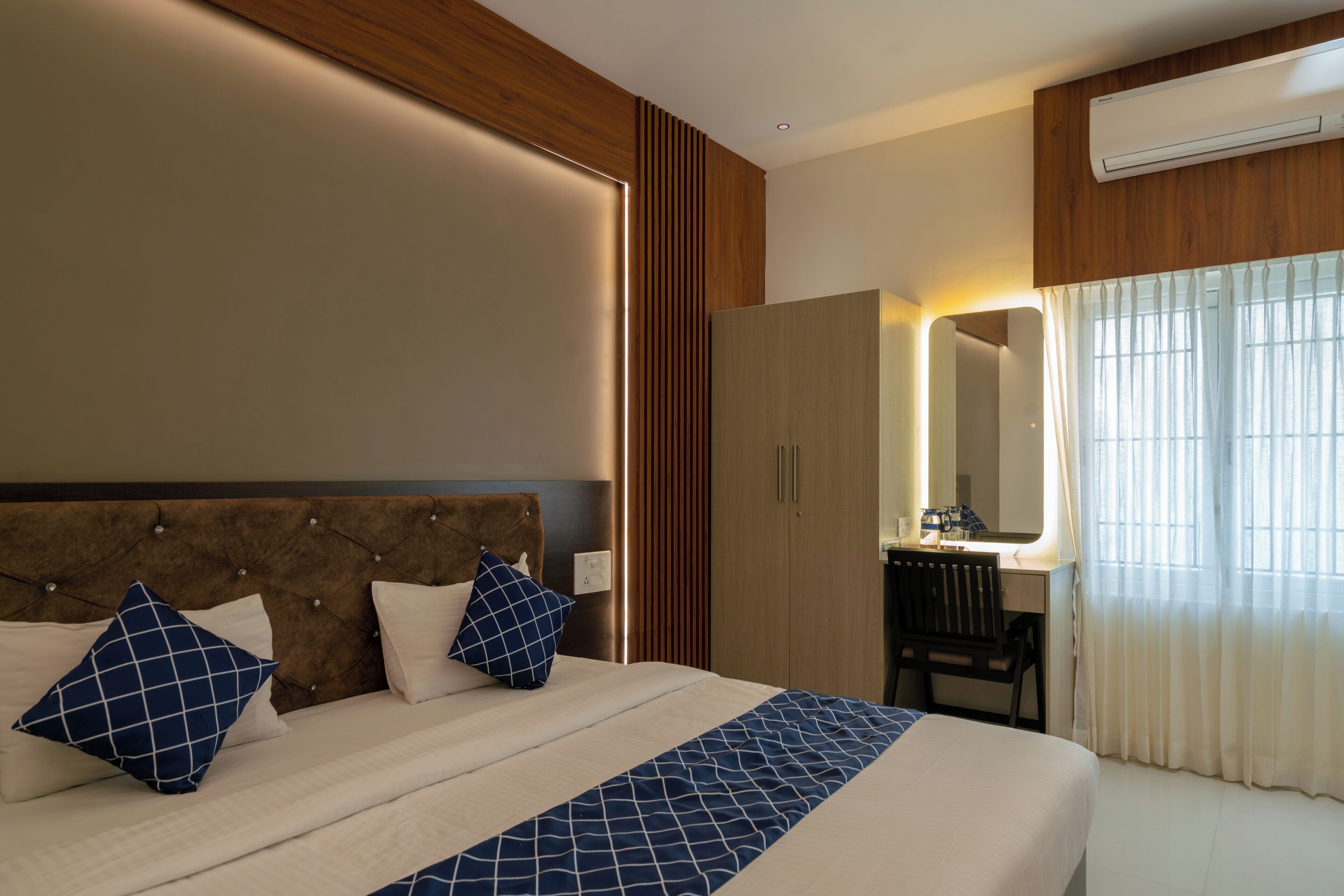 A hotel room with a large bed, a wooden headboard, a desk with a chair, and a mirror.