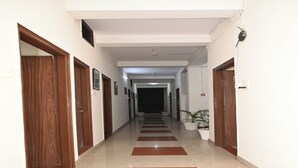 A hotel hallway with wooden doors, a tiled floor with red and white stripes, and a potted plant on the right. - Hotel Aparajita (Varanasi)