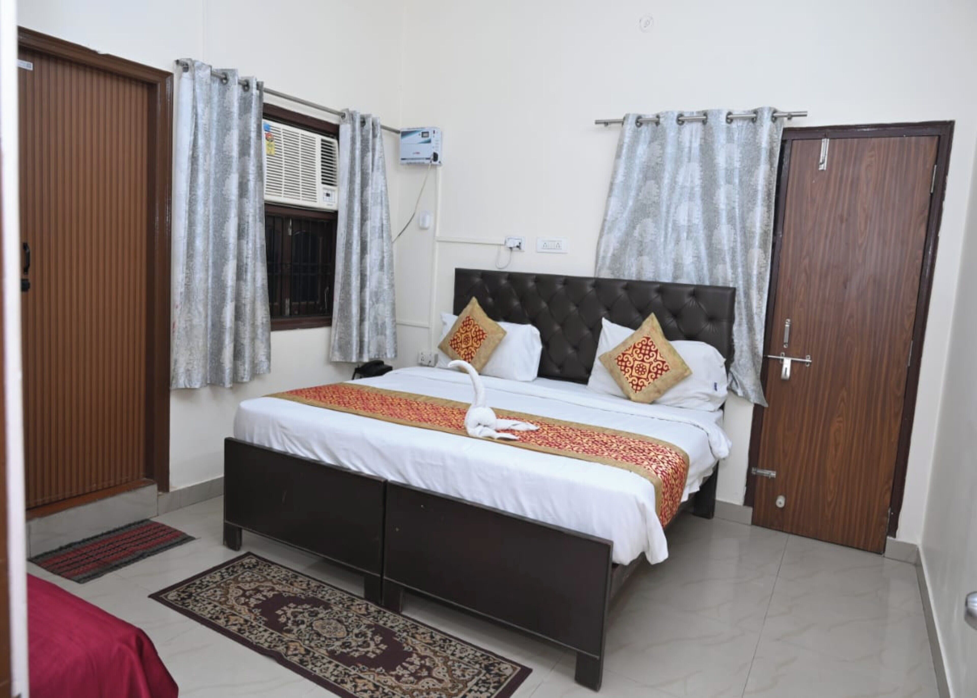 A bedroom with a bed, curtains, an air conditioning unit, and a door.