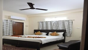 A bedroom with a bed, a ceiling fan, an air conditioning unit, a desk, and a chair. - Hotel Aparajita (Varanasi)