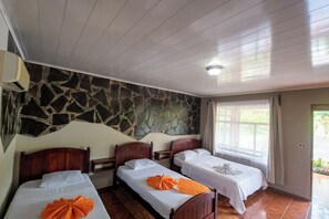 Une chambre d’hôtel avec trois lits en bois, un mur en pierre et une fenêtre avec des rideaux.