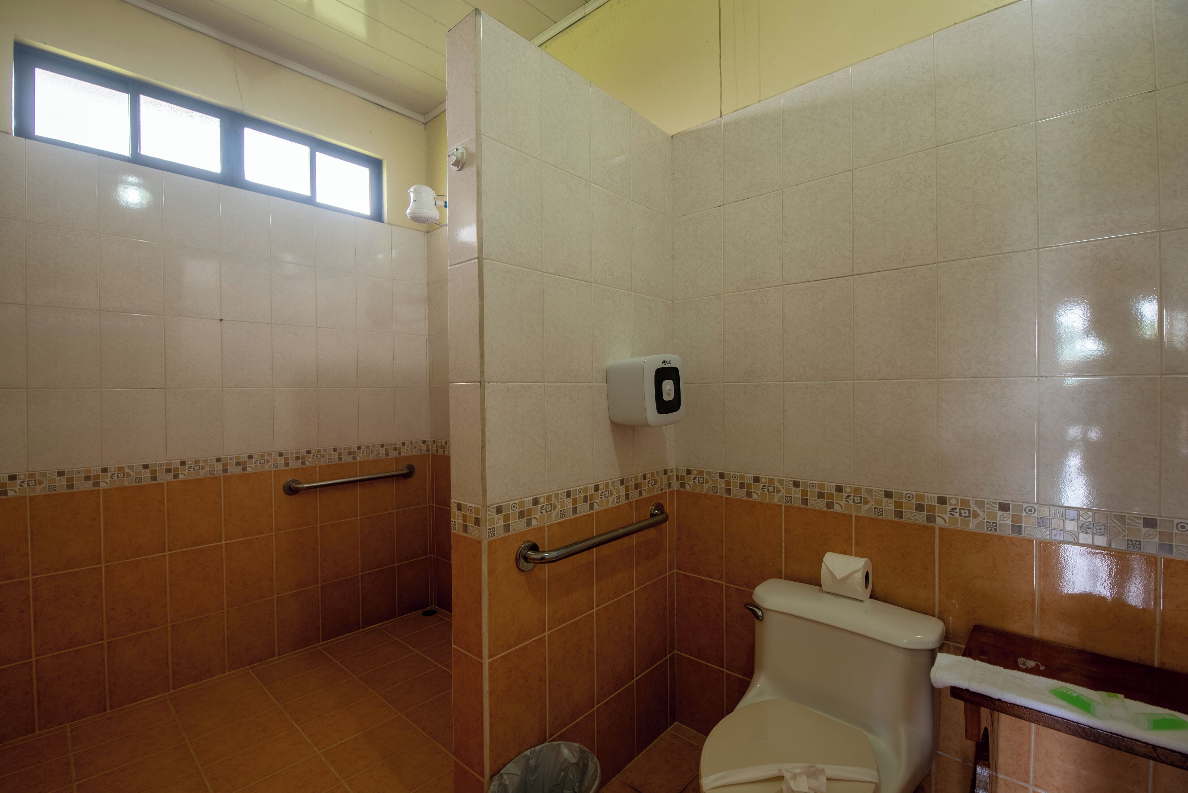 A bathroom with a toilet, a hand dryer, and a trash bin.