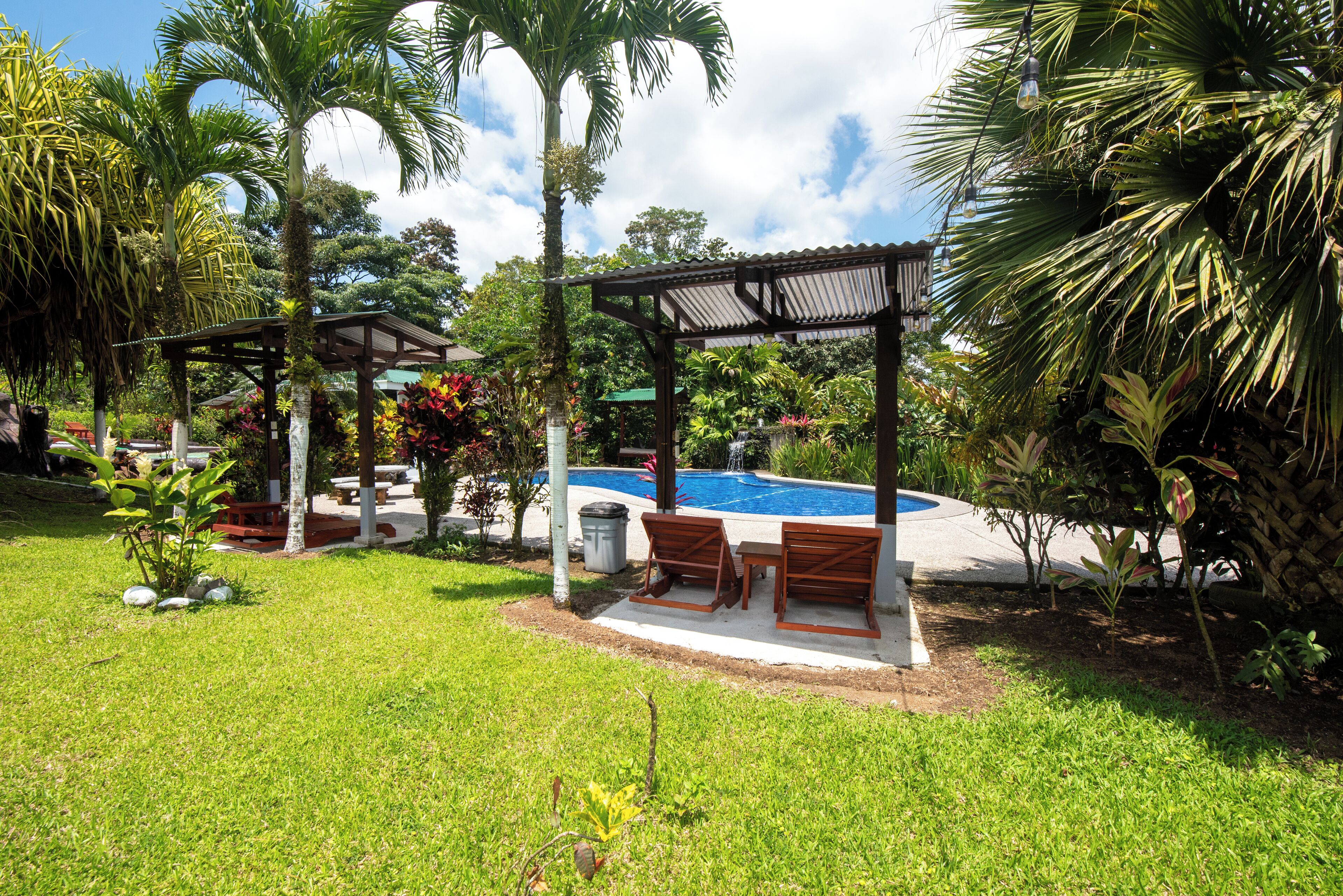 A pool area with a pergola, seating, and lush greenery.