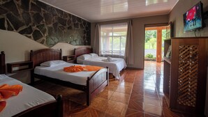 A hotel room with two beds, a stone wall, a TV, and a view of the outdoors. - Sueno Dorado Hot Springs Hotel (La Fortuna)