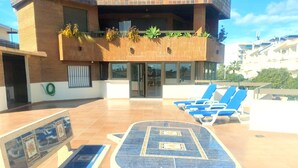 Una terrazza sul tetto con tavolo da biliardo, poltrone relax e un edificio con veranda in legno e piante.