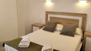 Un letto rifatto con due cuscini, un comodino con una lampada e un punto luce a parete.