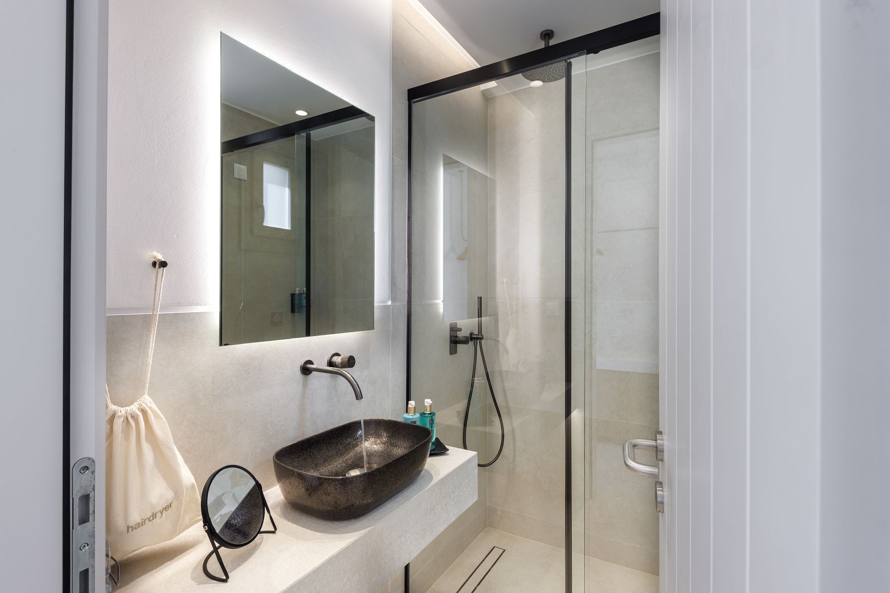 A modern bathroom with a large mirror, a round sink, and a glass shower enclosure.