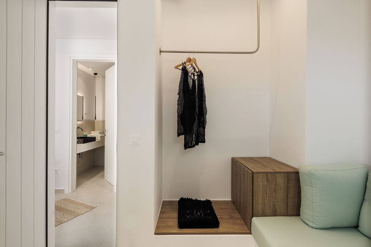 A modern, minimalist bathroom with a walk-in shower, a wooden bench, and a hanging clothes rack.