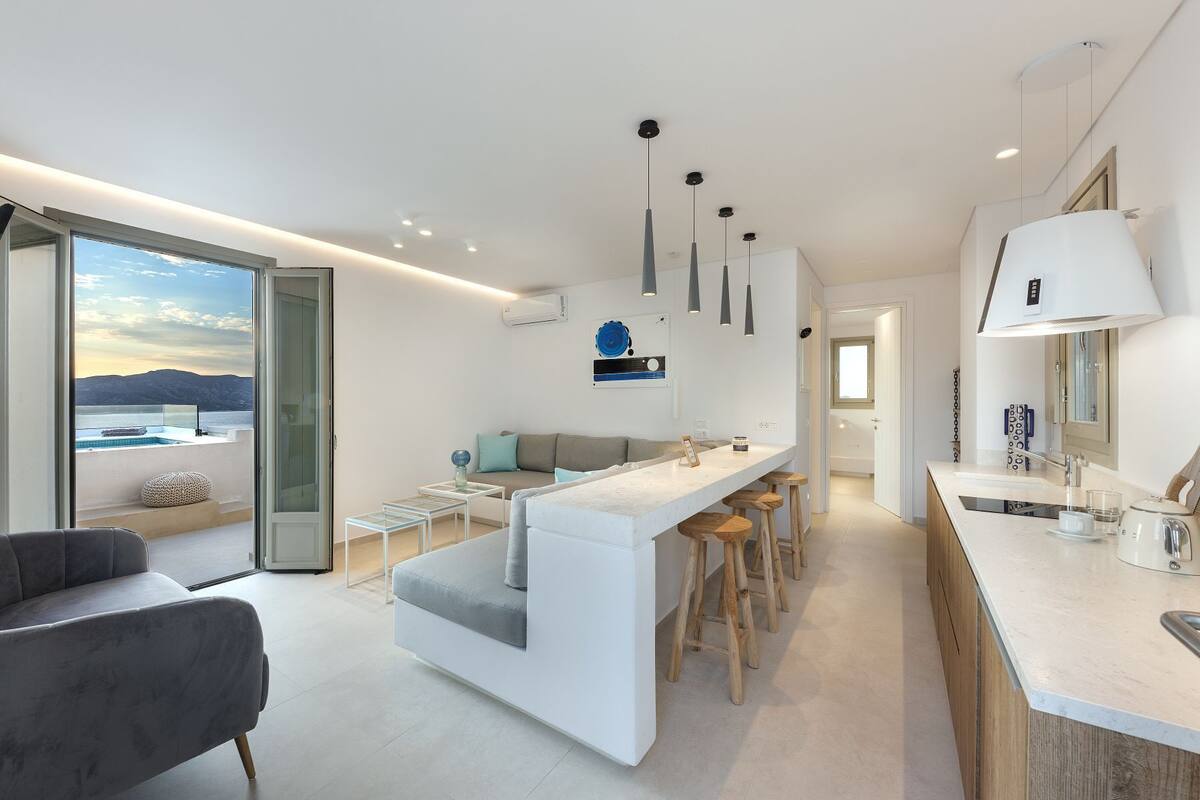 A modern kitchen with a central island, bar stools, and a view of the sea.
