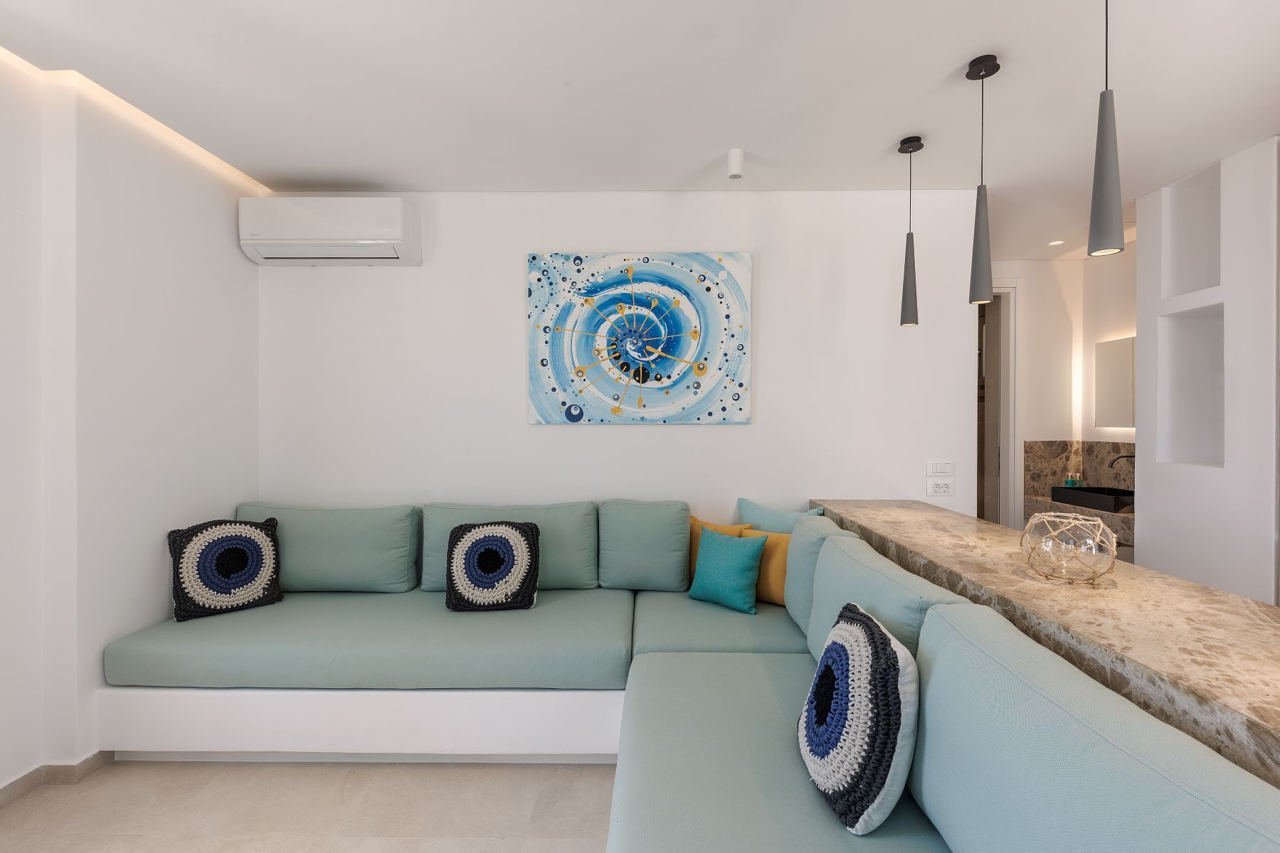 A modern living room with a light green sectional sofa, a large abstract painting, pendant lighting, and a marble countertop.