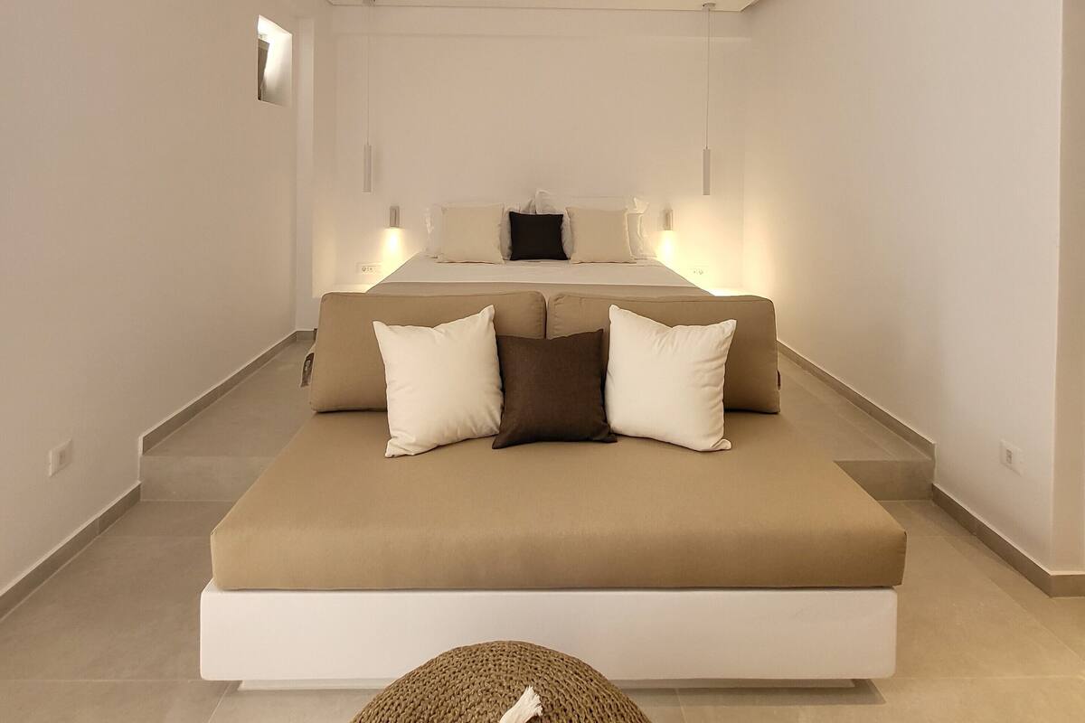A modern bedroom with a large bed, a sofa bed, and a small round ottoman.