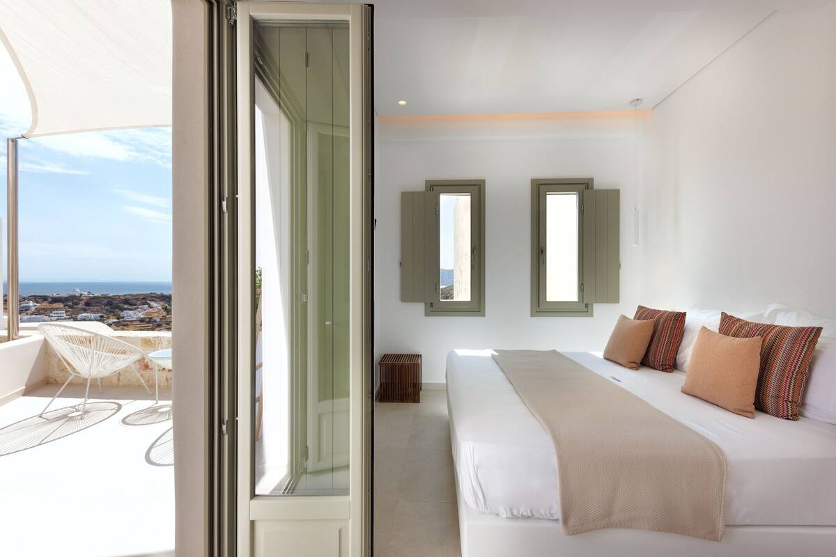 A bedroom with a bed, two windows, and a view of the landscape.