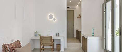 Un dormitorio moderno con cama, escritorio y silla. Hay una puerta que da a un baño y un pasillo.