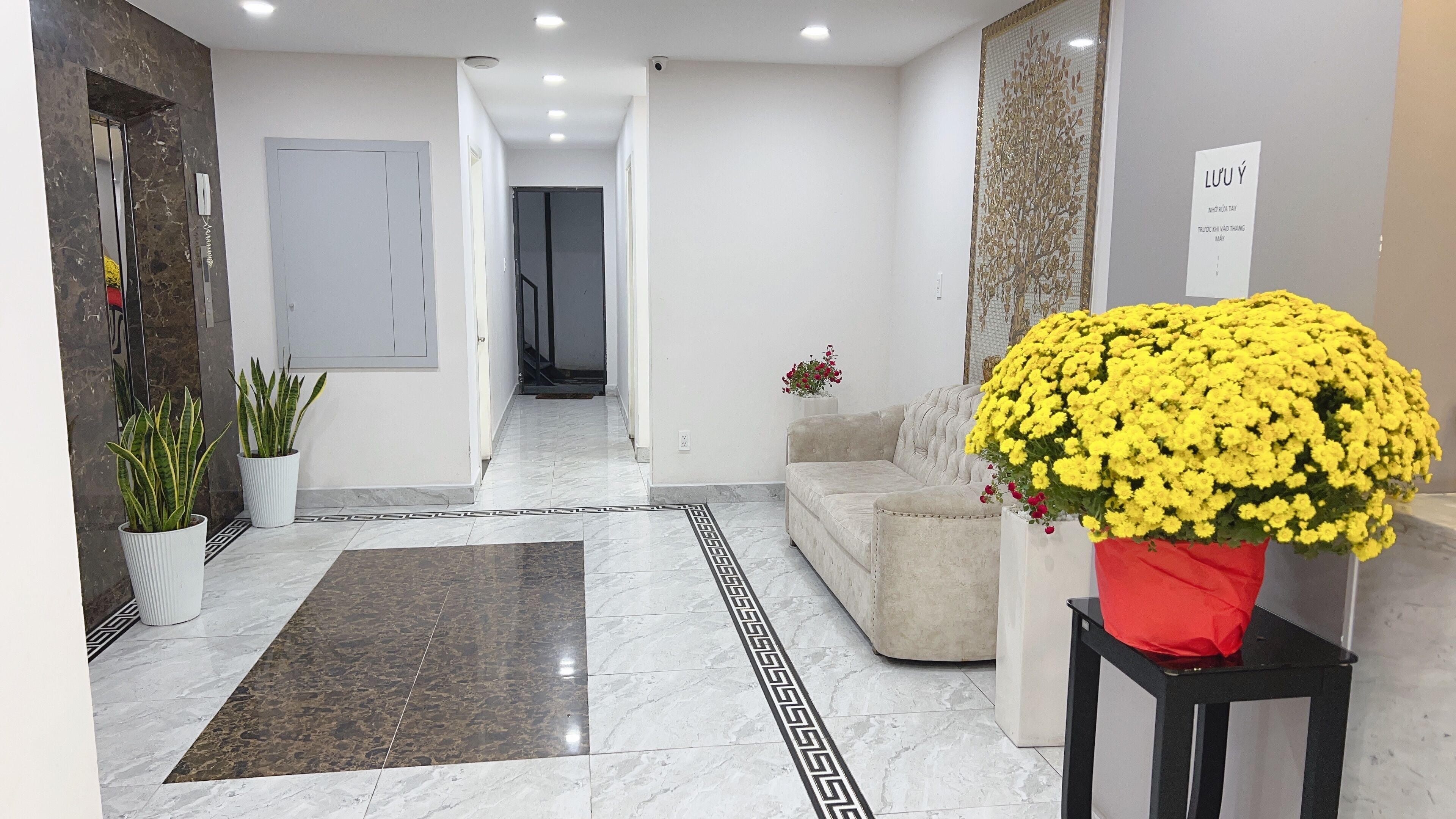 A hotel lobby with a marble floor, a sofa, a coffee table, and a large yellow flower arrangement.