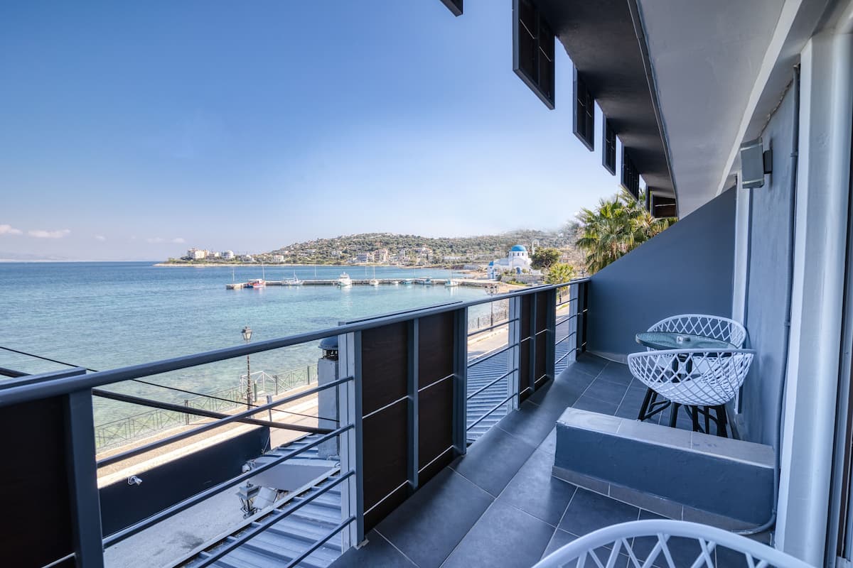 A balcony with a view of the sea, a white chair, and a small table.