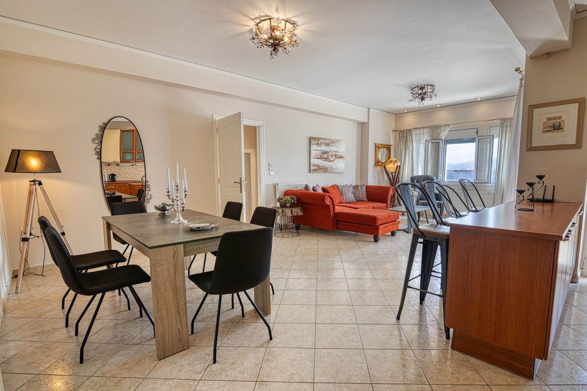 A spacious living area with a dining table, black chairs, a red sofa, and a kitchen area with a wooden cabinet and a bar counter.