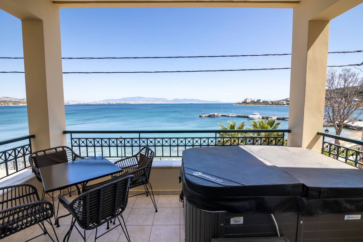 A balcony with a view of the sea, a grill, and outdoor furniture.