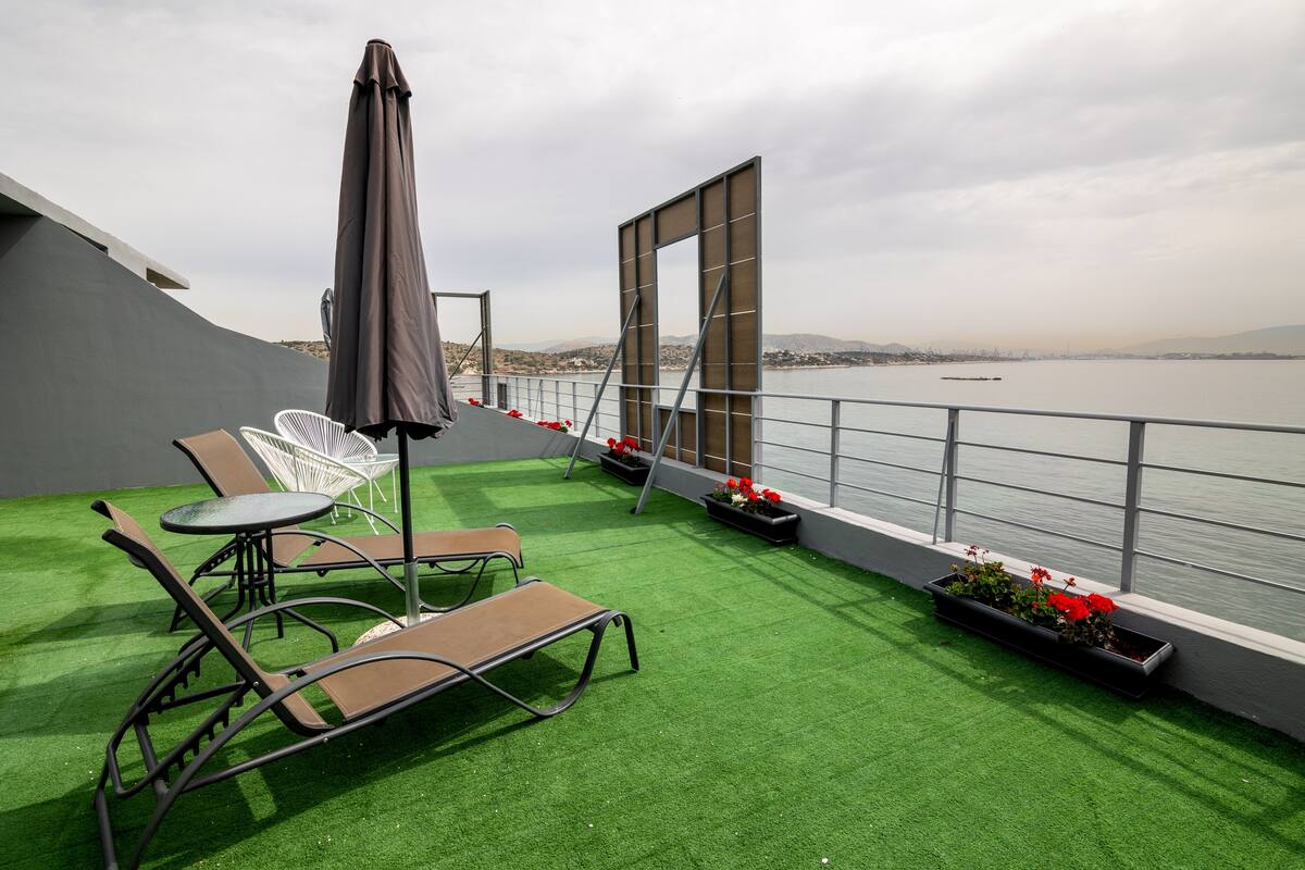 A balcony with artificial grass, a table, two lounge chairs, an umbrella, and flower planters.