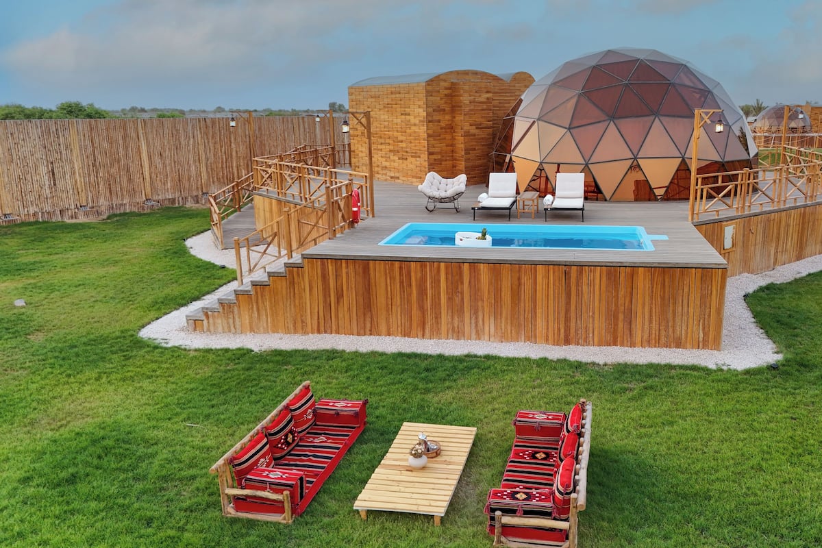 Eine Holzterrasse mit Pool, Liegestühlen und einer roten Sofagarnitur.
