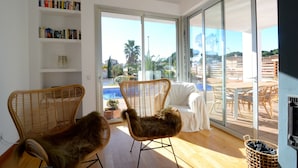 A modern living room with wicker furniture, a white sofa, and a glass door leading to an outdoor patio with a pool. - VILLA PONENT (L'Escala)
