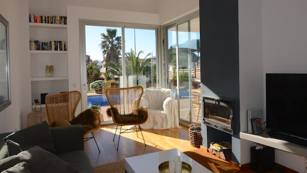 A modern living room with a sofa, a wicker chair, a fireplace, a television, and a bookshelf. - VILLA PONENT (L'Escala)
