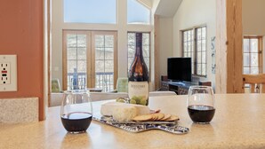 Une cuisine avec une bouteille de vin, du fromage, des crackers et des verres de vin rouge posés sur le comptoir.
