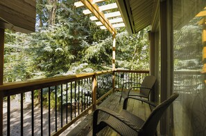 A wooden deck with a railing, two wicker chairs, and a view of snow-covered trees.