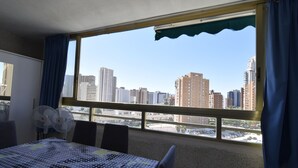 A room with a large window, a table with a patterned tablecloth, and two fans. - MARISCAL 6 (1 BEDROOM) (Benidorm)