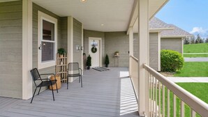 A covered porch with a railing, two chairs, a small table, and potted plants. - Majestic Mountain Views! (Kalispell)