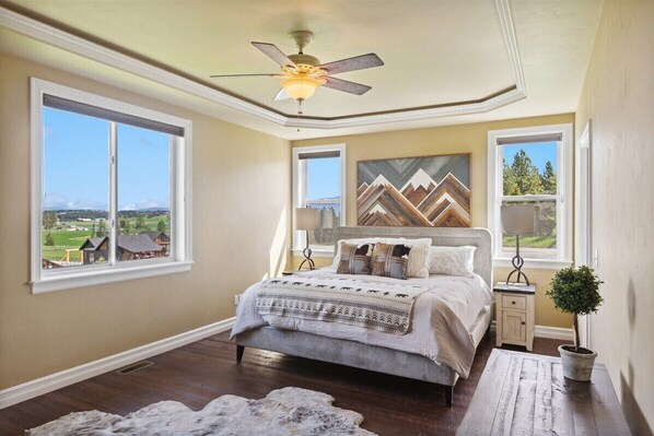 Une chambre à coucher avec un lit, un ventilateur de plafond, une fenêtre donnant sur un beau paysage, une table de chevet et une plante en pot.