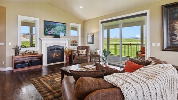 A spacious living room with a fireplace, comfortable seating, a television, and a large window offering a view of the outdoors. - Majestic Mountain Views! (Kalispell)