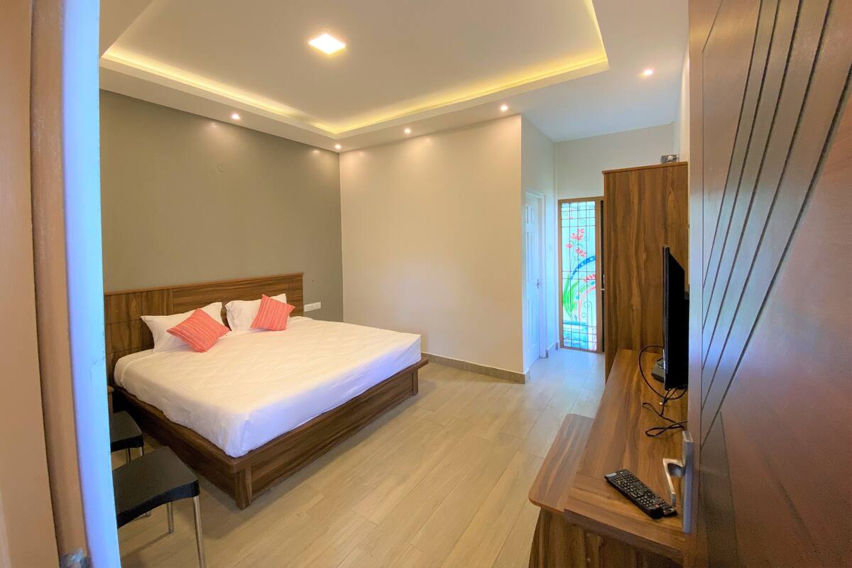 Un dormitorio moderno con una cama de madera, un escritorio con televisor y un ventanal de vidrio emplomado.
