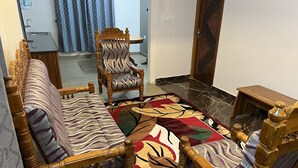 A living room with a sofa, a wooden chair, a patterned rug, and a dining table. - AVALON STAYS  OOTY (Ootacamund)