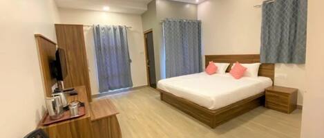 A hotel room with a bed, bedside table, desk, chair, and a television.