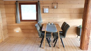 Ein Zimmer mit Holzvertäfelung, einem Tisch mit Stühlen, einem Fenster mit Vorhängen, einem kleinen Regal mit Büchern und einer Topfpflanze.