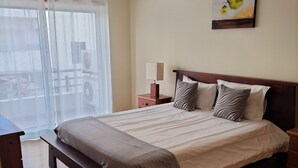 Ein Schlafzimmer mit einem hölzernen Bett, einem Nachttisch, einer Lampe und einem Fenster mit transparenten Vorhängen.