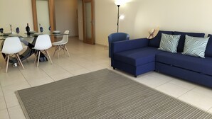 Ein Wohnzimmer mit einem blauen Sofa, einem Esstisch mit Stühlen und einem gemusterten Teppich.