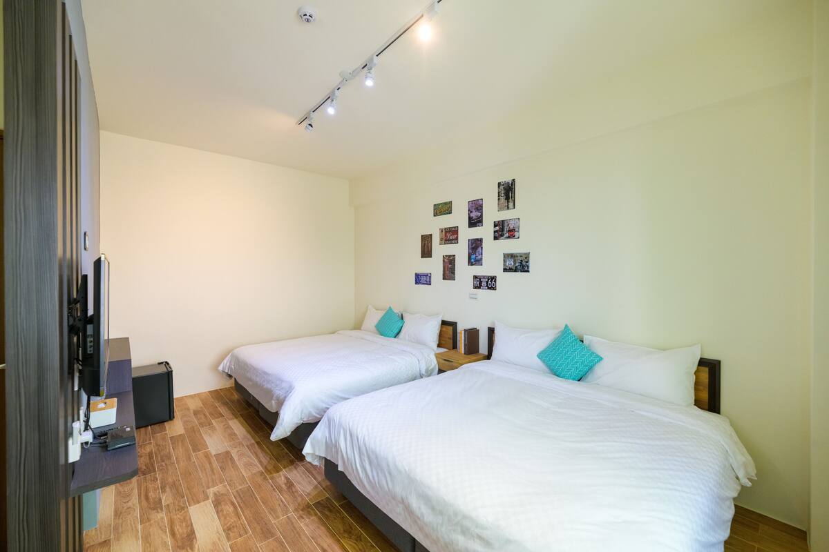 A hotel room with two beds, a flat-screen TV, and a wall decorated with photos.