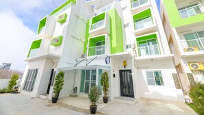 Um edifício moderno de vários andares com fachada branca e verde, janelas grandes e telhado plano.
