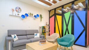 Uma sala de estar moderna com um sofá cinza, uma mesa de centro de madeira e uma poltrona azul-esverdeada. Há uma estante com livros e objetos decorativos.
