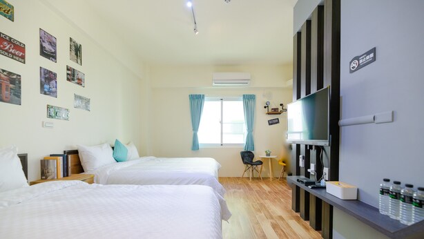 Quarto de hotel com duas camas, televisão, escrivaninha com computador e janela com cortinas.