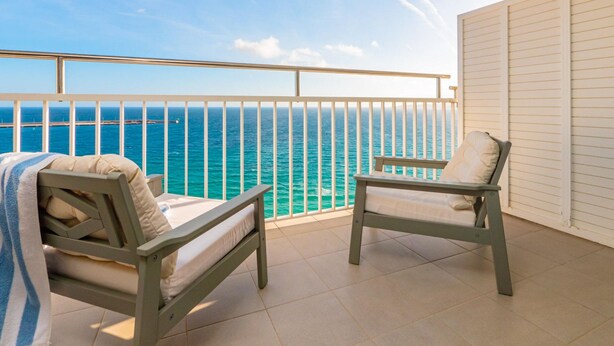 A balcony with two wooden chairs and a bench, overlooking a turquoise sea and a clear sky. - Cozy Beachfront Apartment in Palamós (Palamós)