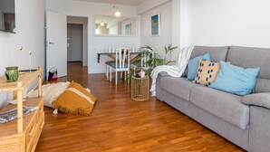 A modern living room with a grey sofa, wooden flooring, and a dining area with a white table and chairs. - Cozy Beachfront Apartment in Palamós (Palamós)
