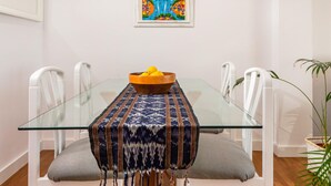 A dining table with a glass top, surrounded by white chairs, and a woven table runner. - Cozy Beachfront Apartment in Palamós (Palamós)