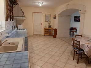 Una cocina con lavabo, estufa y suelo de baldosas. Hay una mesa de comedor con sillas y un mueble pequeño.